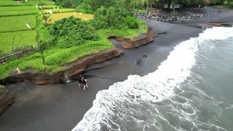 Walking along the black coast in cloudy weather, the drone follows people Stock Footage 231691935