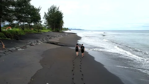 Walking along the black coast in cloudy weather, the drone follows people Stock Footage 231693881