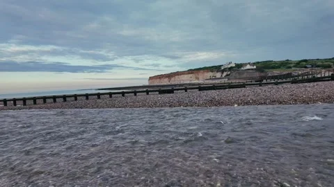 Walking along quiet pebble beach with sea groynes and coastal cliffs Stock Footage 309767273
