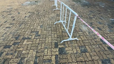 Walking along White Crowd Control Barriers tied Warning Tape on Wet Cobblestone. Vidéo 342369798