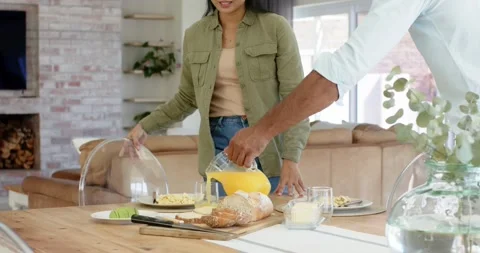 Walking to breakfast table in kitchen, Diverse couple pulling chairs, pouring Stock Footage 339413001