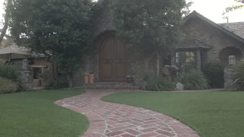 Walking up a brick path to a stone cottage with an arched door Stock Footage 345546022