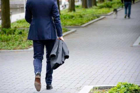 Walking businessman on sidewalk in a park. Businessman in blue business suit Stock Photos