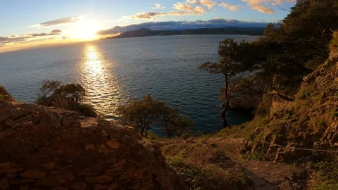 Walking down stairs down a rocky cliff overlooking the sea at sunrise. Plants Stock Footage 141808341