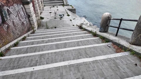 Walking down stairs on the side of a river bank towards a vandalised scooter 動画素材 342391167