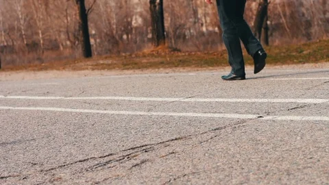 Walking feet on pavement.A young man in black pants and a black jacket walks by Stock Footage