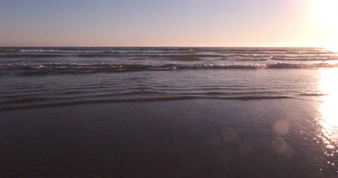Walking forward through shallow waves breaking on flat beach at sunset. POV. Stock Footage 135368968