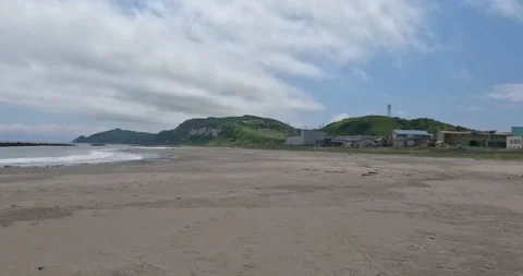 Walking on a grey sand beach with many shells green mountains at the horizon 스톡 동영상 255104063