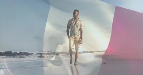 Walking man in patterned short-sleeve shirt, shorts on wet sand, with faint Stock Photos