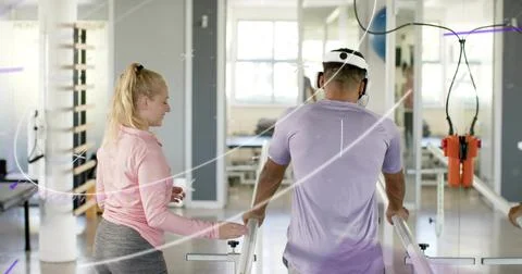 Walking man in purple tee using parallel bars in rehab gym, therapist guiding Stock Photos