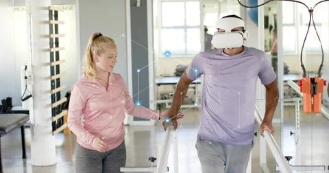 Walking man in purple tee, VR headset taking steps in therapy gym, assistant  Fotos Stock