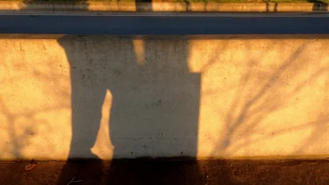 Walking man shadow on the concrete fence. Yellow sunlight and contrasting Stock Footage 123121753