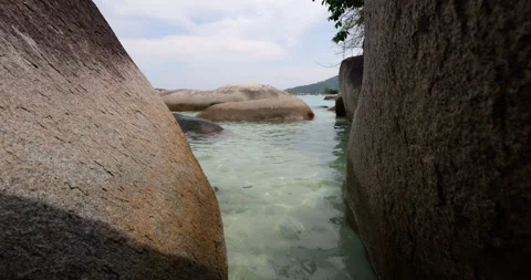 Walking in narrow aisle between large rocks to shallow sea shore Stock Footage 314637348