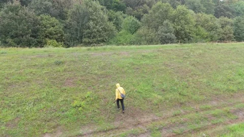 Walking on a narrow path through fields and forests, a man in a yellow rain.. Stock Footage 286308243