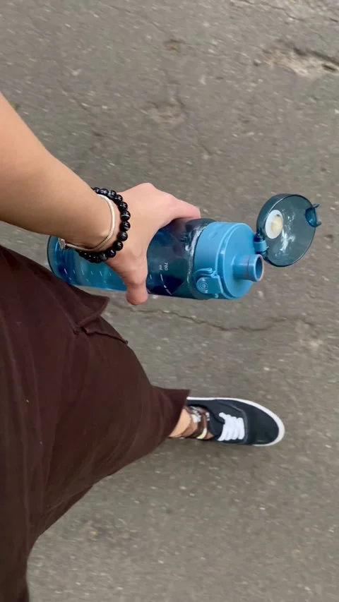 Walking with Open Blue Water Bottle on City Street Stock Footage 304544506