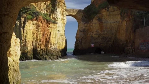 Walking out of a cave to secret beach and stone bridge over cliffs Stock Footage 273675701