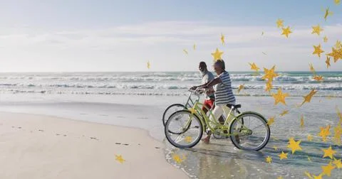Walking pair pushing green bikes on beach barefoot prints waves gold-star Fotos Stock