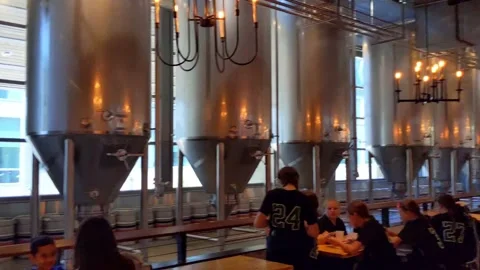 Walking past diners sitting next to a row of huge beer fermentation tanks Vídeo Stock 226431902