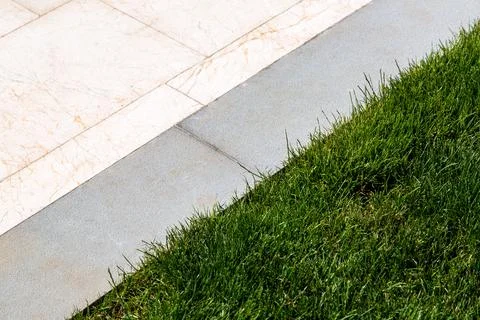 Walking path of beige marble and gray curb in the pavement and green lawn. Stock Photos