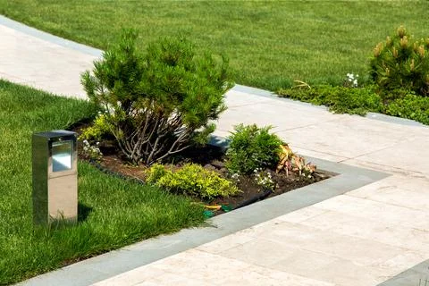 Walking path of marble tiles and stone edges in the garden with a green lawn. Stock Photos