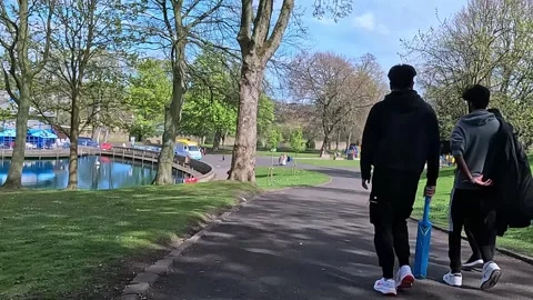 Walking path through lush green trees near the lake in Lister Park, Bradford Stock Footage 333072414