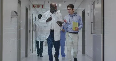 Walking physicians in white coats pointing at tablet in hospital corridor, Stock Photos