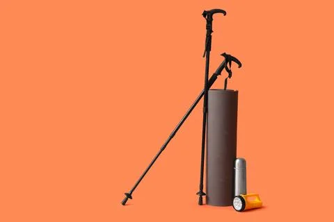 Walking poles with mat, flashlight and thermos on orange background Stock Photos