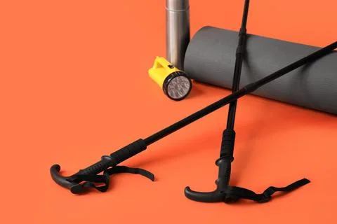 Walking poles with mat, flashlight and thermos on orange background Stock Photos