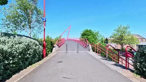 Walking POV approach to the red Peace Bridge in Bradford, UK Видео 333794229