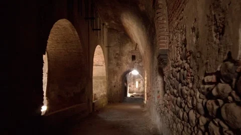 Walking POV through ancient stone corridor with arches and light at end Stock Footage 334629414