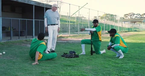 Walking senior coach instructing Diverse baseball players by dugout, teaching Stock Footage 344333035