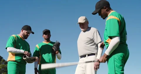 Walking onto sunlit baseball field senior coach briefing players on positions Stock Footage 339271740