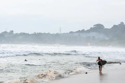 Walking surfer enjoy cloudy sunset near the beach with sea mist everywhere Stock Photos