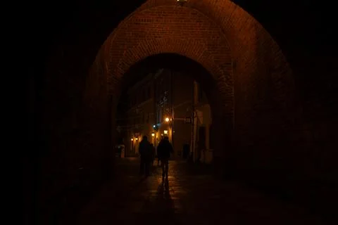 Walking through a brick archway in a quiet town at night with warm lights Stock Photos