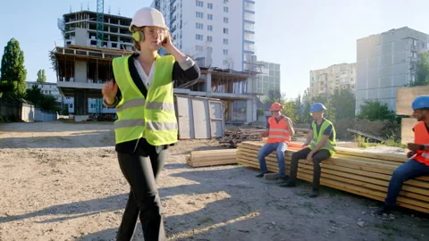 Walking through the construction site beautiful engineer lady to her team of Stock Footage 146605408