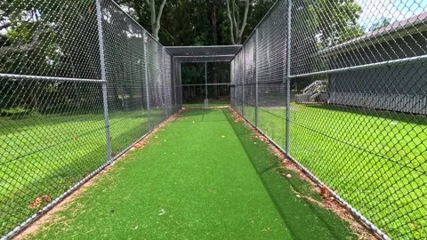 Walking through empty outdoor cricket net with green turf and chain-link fe.. Stock Footage 332590366