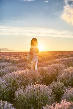 Walking through lavender rows at sunset. Young beautiful woman in dress standing Stock Photos