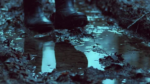 Walking through a muddy puddle in rubber boots on a forest road in the evening. Stock Footage 239862714