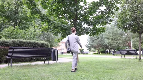 Walking through serene park filled with trees and benches in afternoon sunlight Stock Footage 297181063