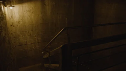 Walking towards the stairs and down a dimly lit concrete stairwell Видео 301030052