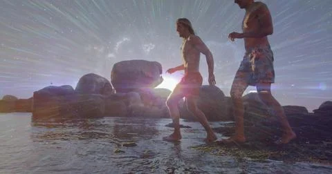 Walking two shirtless men in trunks crossing wet rocky shore with granite Stock Photos