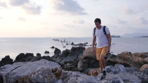 Walking widely with a backpack behind your back along large stones near the sea Stock Footage 93801625