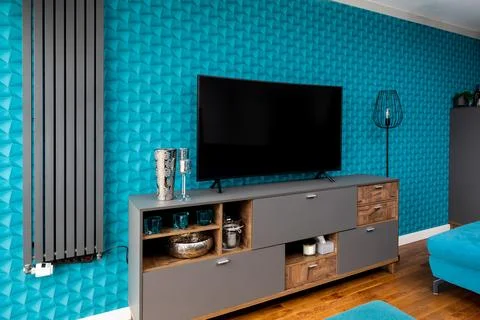 A wall with blue patterned wallpaper. A modern gray radiator. A dresser wit.. Stock Photos