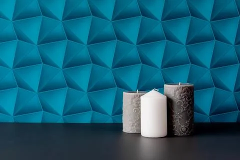 A wall with blue patterned wallpaper. Three candles, one white, the rest gray Stock Photos