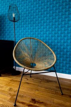 A wall with blue patterned wallpaper. Wicker chair on black metal legs. Woo.. Stock Photos