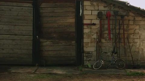 On wall of brick barn with large gates hang shovels, pitchforks, crowbars and Vidéo 317227797