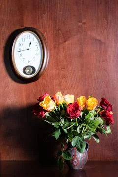 Wall clock and fresh red and yellow roses in jug Stock Photos
