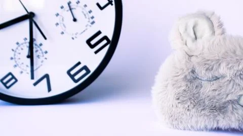 Wall clock on the back white background and a fluffy sleeping mask Stock Photos