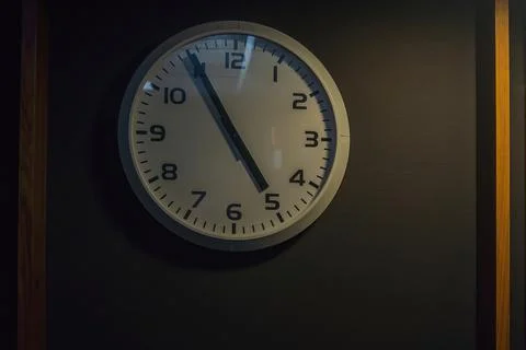 The wall clock on the gray wall shows five to five o'clock Stock Photos