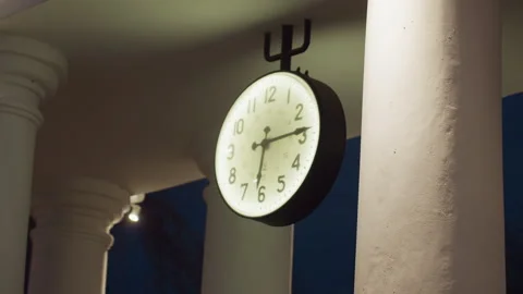 Wall Clock Hanging Under Roof Surrounded by White Pillars at Night Stock Footage 307723534